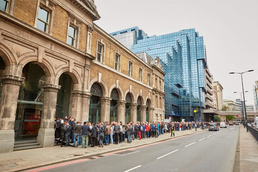 A packed line of people waiting outside a stone-arched building, the Old Billingsgate Market. 