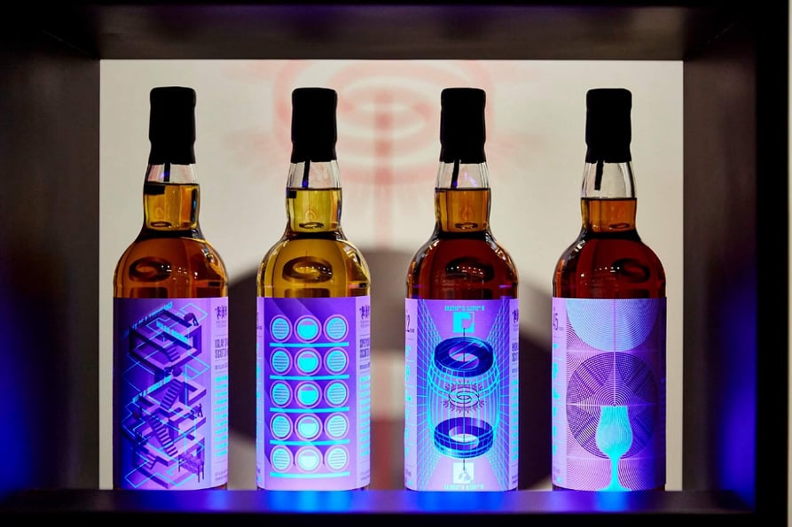Four whisky bottles on a dark shelf and illuminated in electric blue.