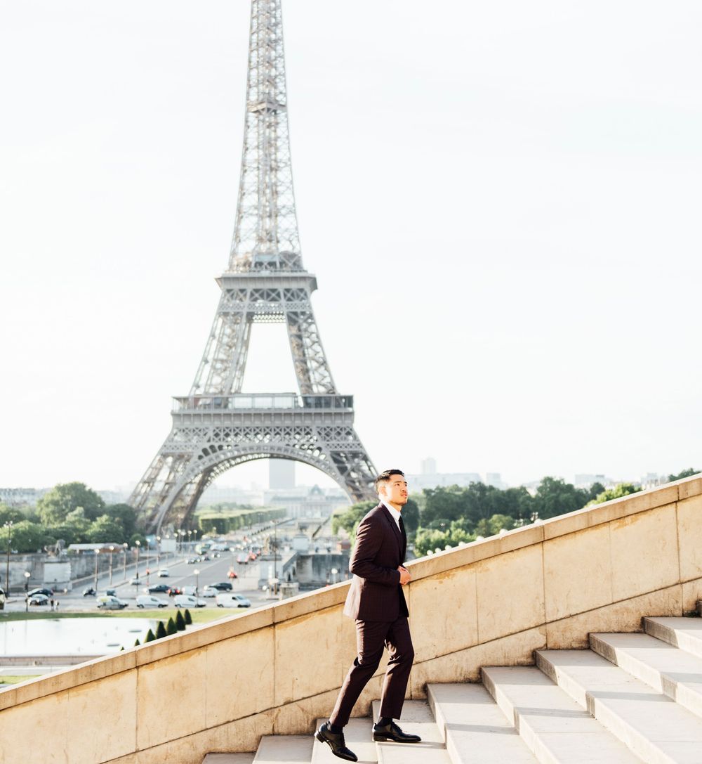 Luxury travel influencer, Cameron Lee, climbing a flight of steps in a black suit with the Eiffel Tower in the background.