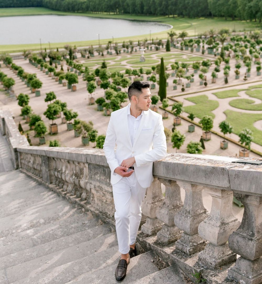 Travel influencer, Cameron Lee, stood in a white suit on a flight of stone stairs with the Orangery Gardens in the background.
