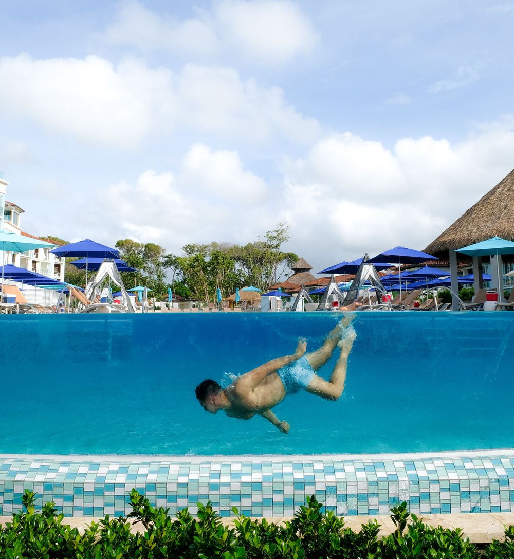 A shot of travel influencer, Cameron Lee, swimming underwater. The photograph is taken through the pool's transparent side wall.