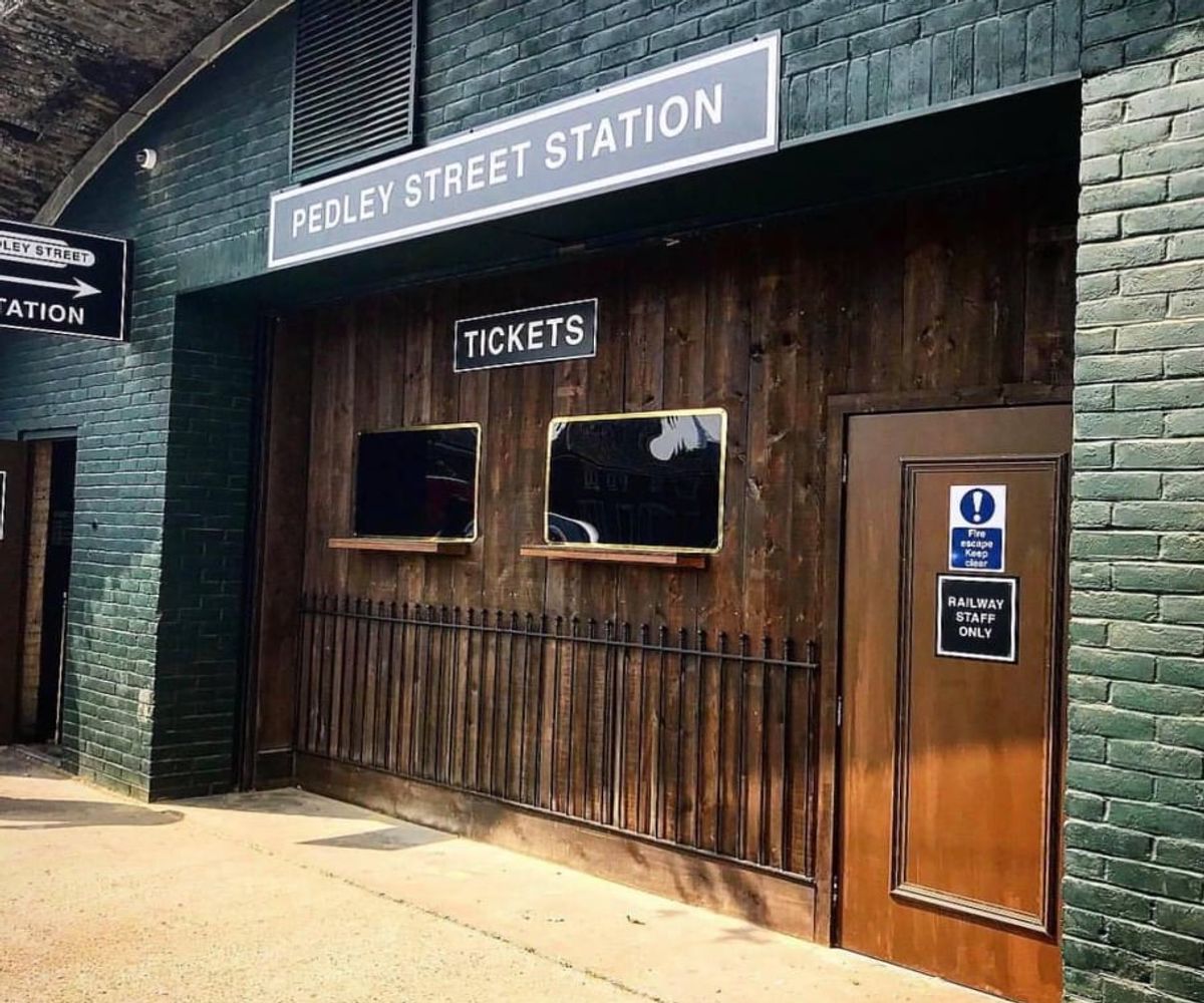 The exterior of The Murder Express, London's immersive murder mystery dining experience. Wooden paneling recreates a realistic station front, with a ticket sign for added effect.