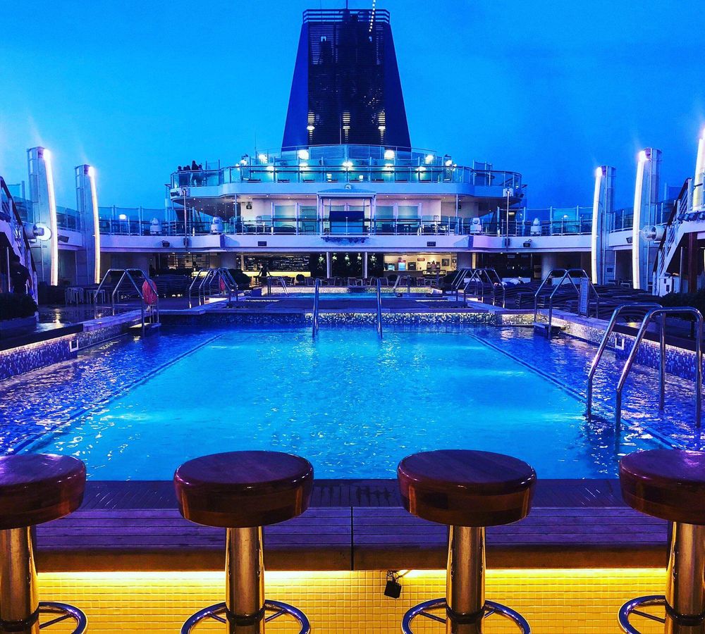 UK cruises can be a great way to unwind and explore the Isles by coast. This image shows the top deck at night, with a swimming pool and illuminated bar stools.