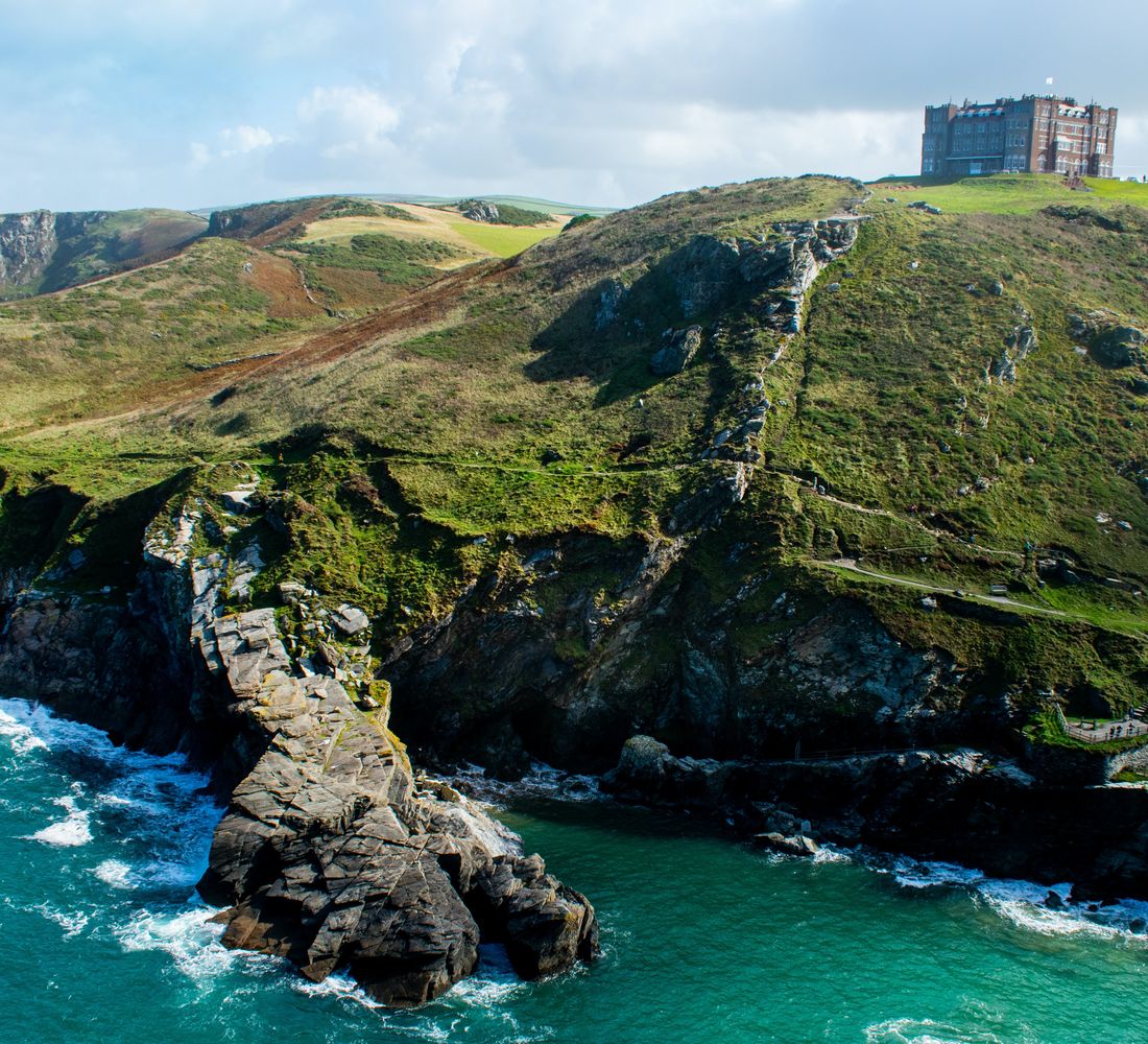 This image shows a harsh, rugged coastline. Dark cliffs drop into the water from the uneven green landscape above.