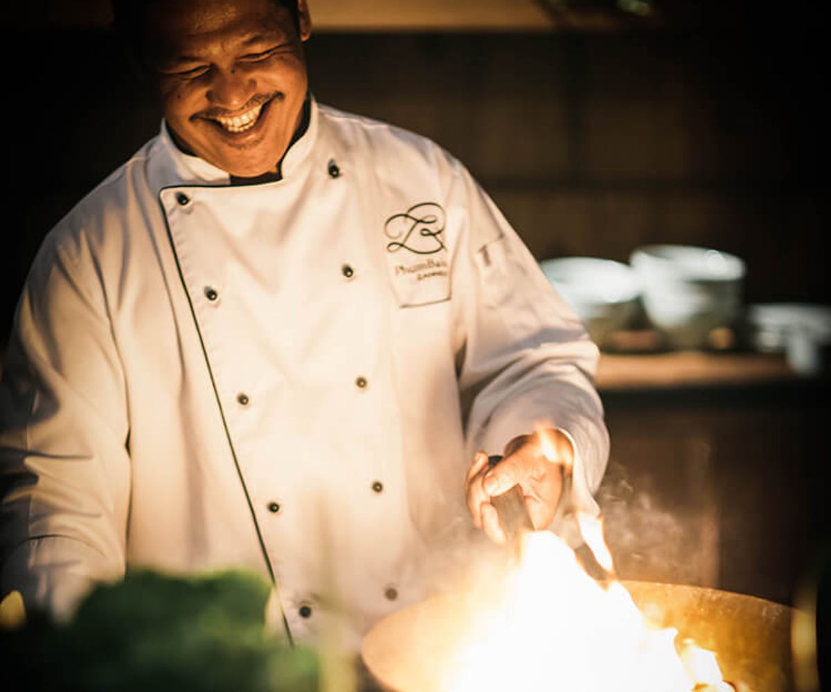 A chef at Phum Baitang smiles as he cooks a flaming dish.