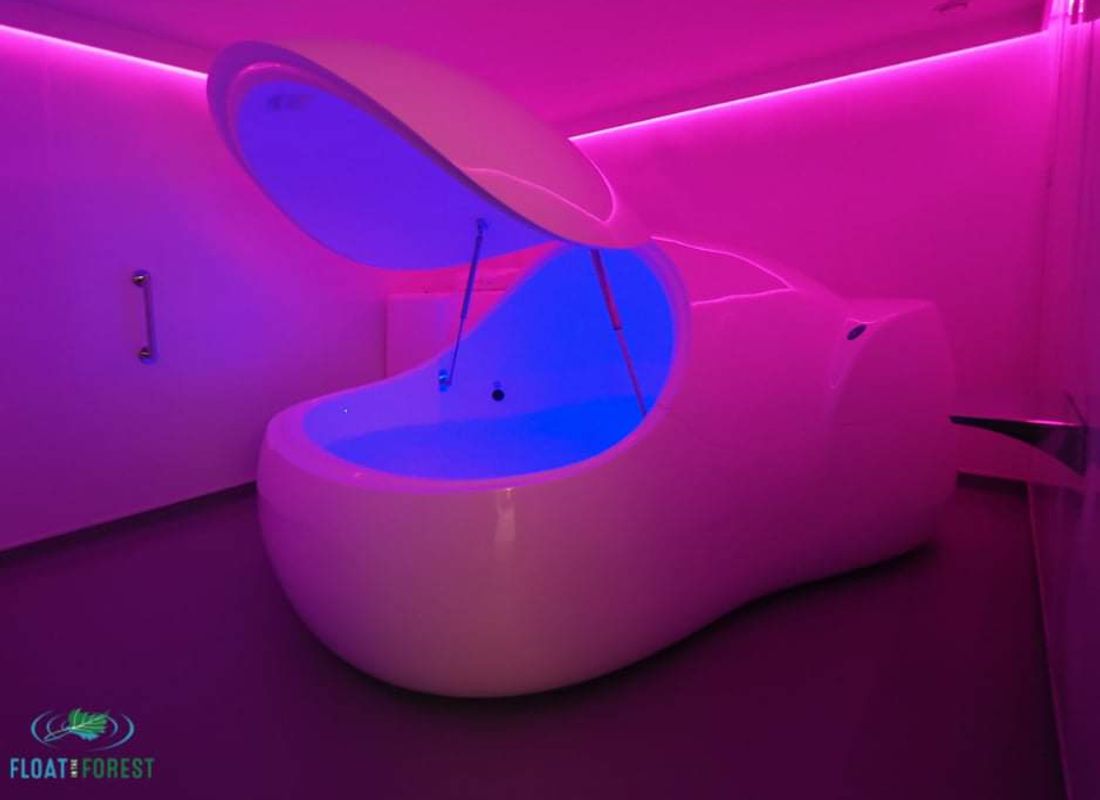 A room filled with pink light with an open floatation tank in the middle.
