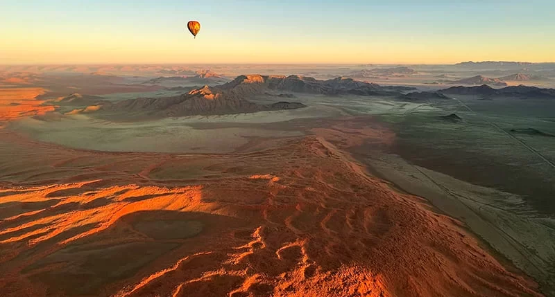 A hot air baloon sails over the red Namib sand.