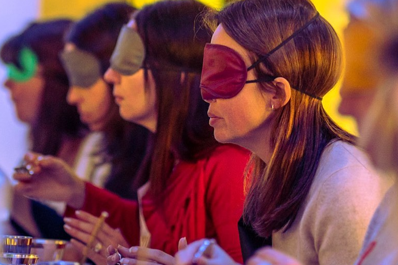 Blindfolded people sitting in a line at a table